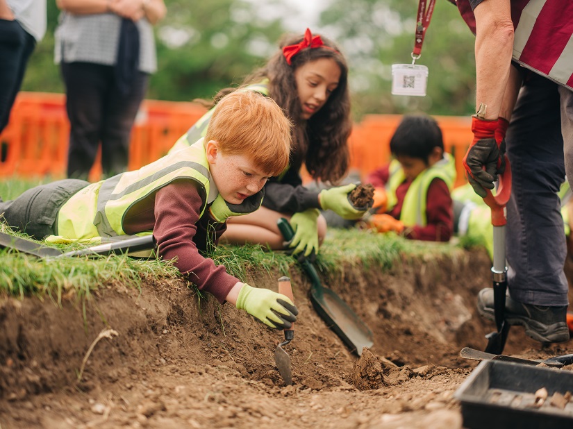 A child lies on the ground over the archaeology dig