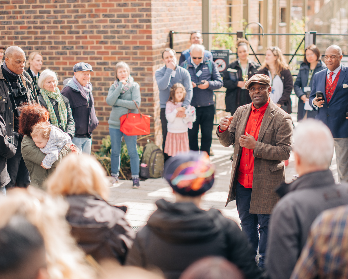 A crowd of people can be seen listening to Paterson Joseph as he reads from his book.