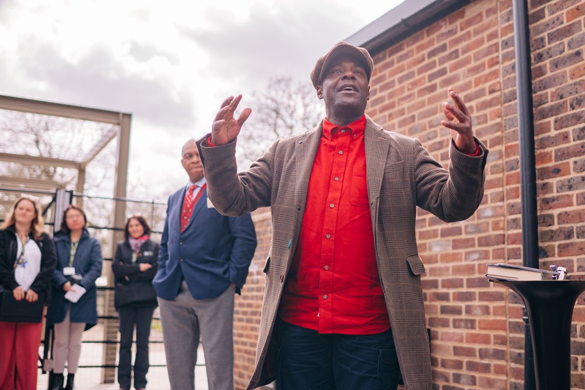 A shot taken from below looking up at Paterson joseph as he gesture with his arms in front of the cafe