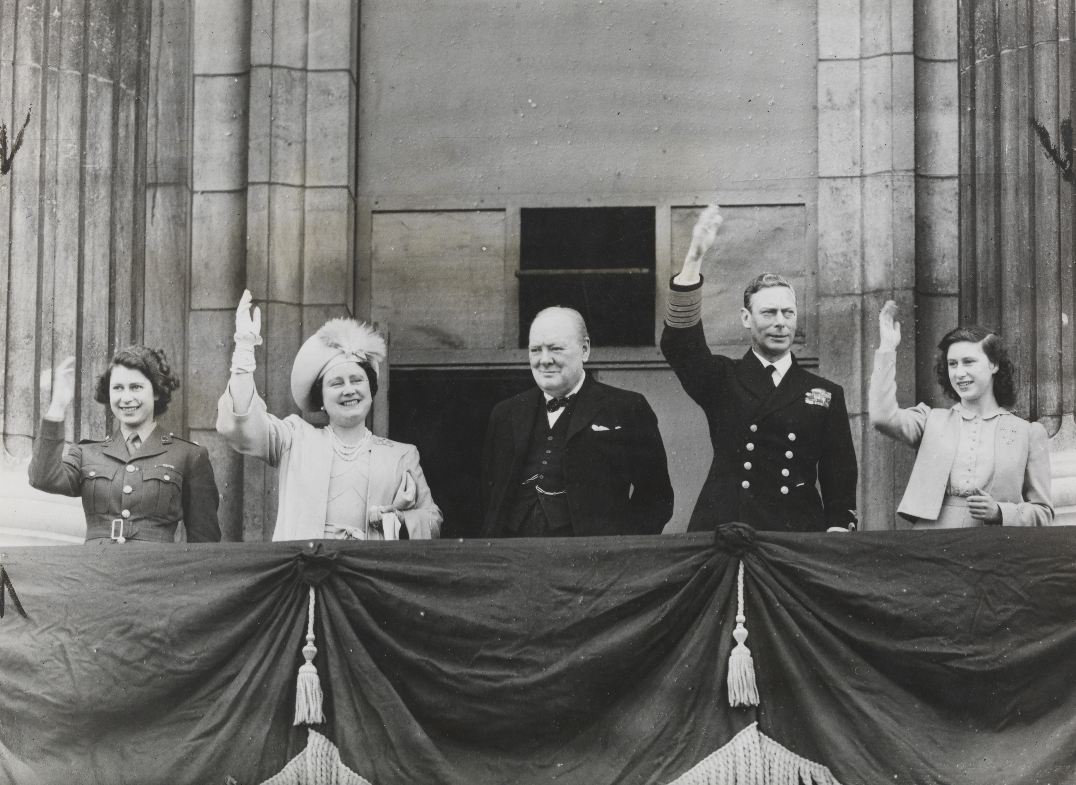 On VE Day, Princess Elizabeth, Queen Elizabeth, Winston Churchill, King George VI and Princess Margaret waves to crowds from Buckingham Palace 