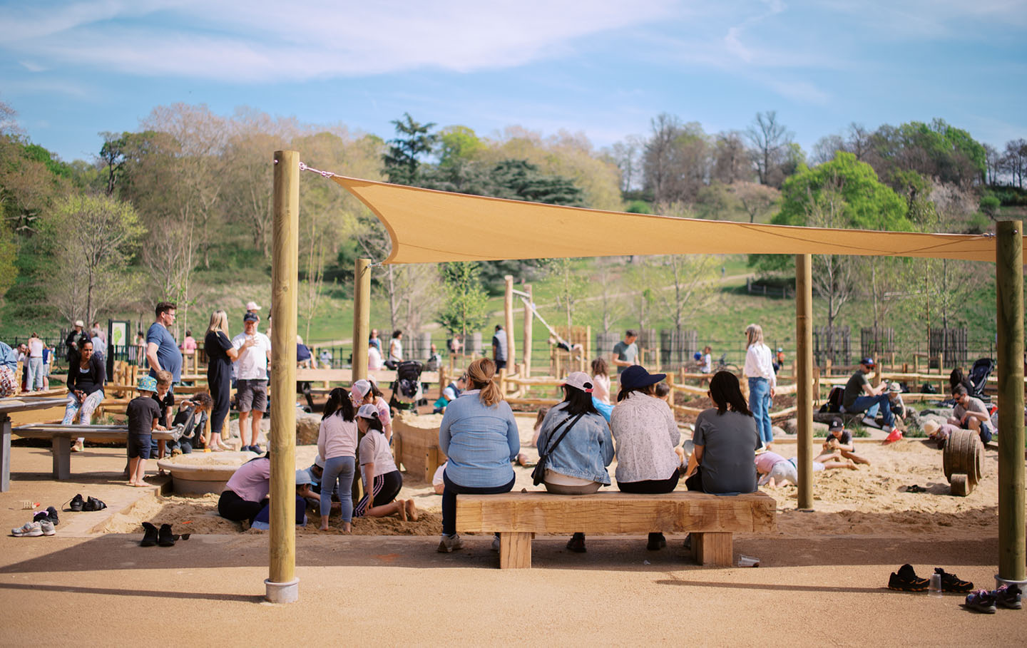 Parents on covered seating watch their children playing in a sandpit
