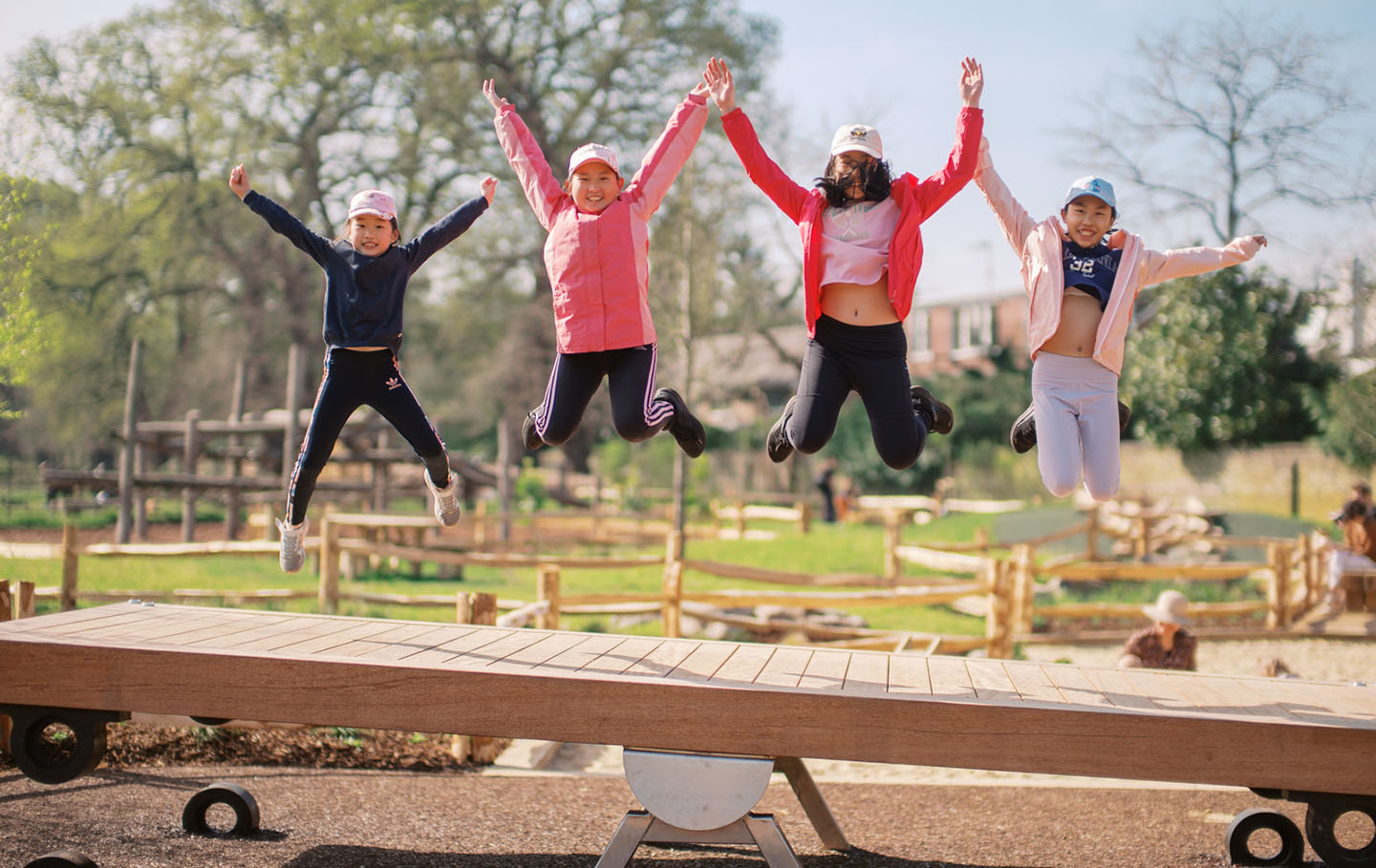 Four girls jumping above a giant see-saw