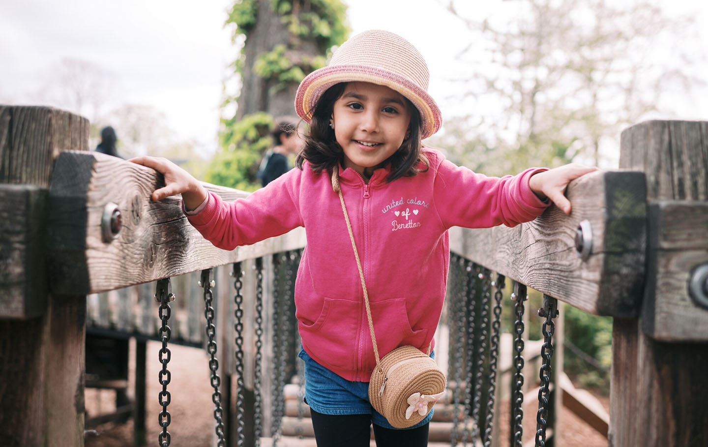 A young girl in a hat crossing a playground bridge