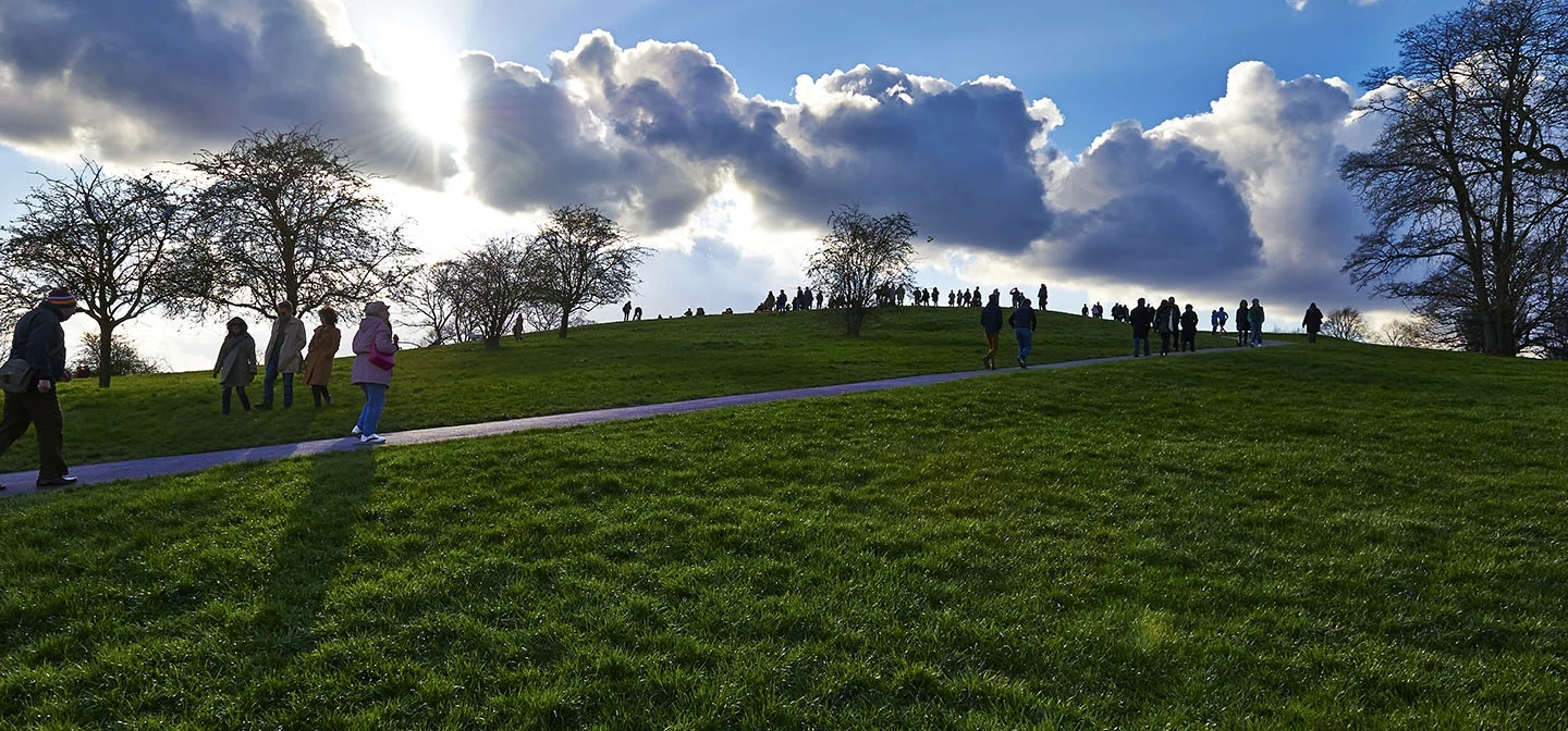The sun setting behind the clouds at the top of a hill