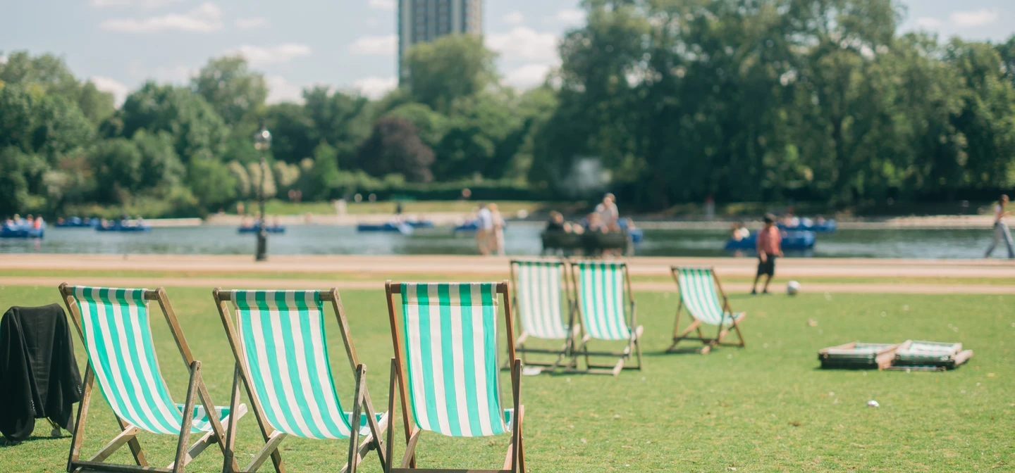 Three deck chairs on a green, grassy patch near a body of water