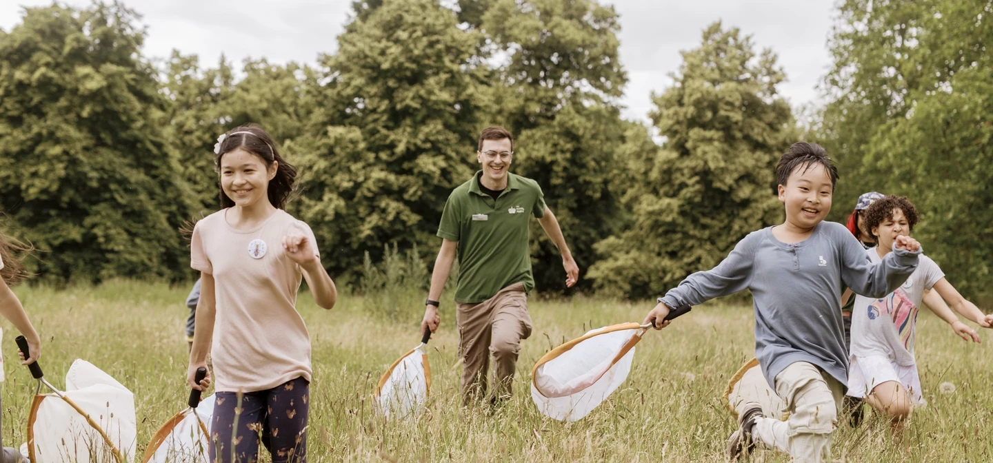 Children and a park ranger running in an open field, with happy smiles and nets in their hands.