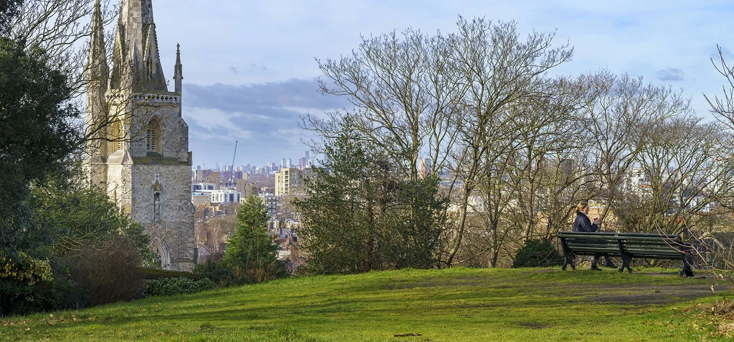 Woman sitting on a park bench, with a church in the background.
