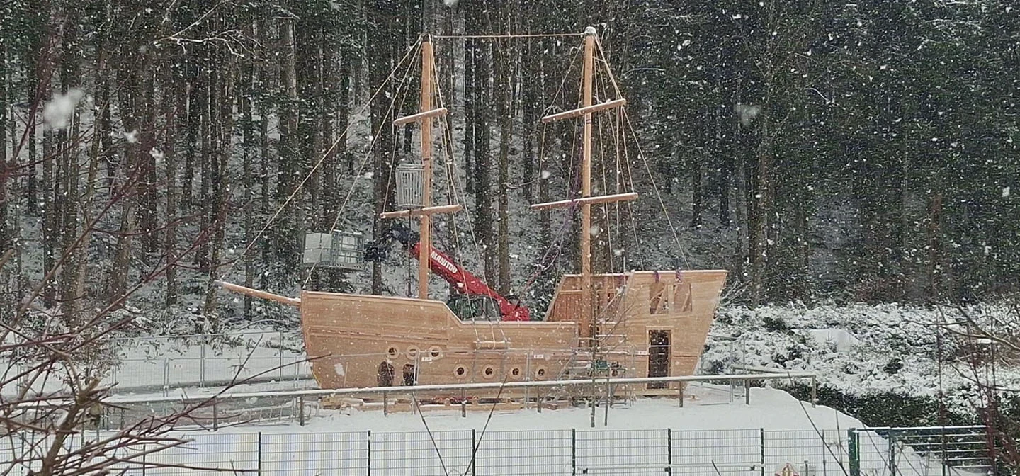 A wooden playground 'galleon' being constructed in front of a snowy forest