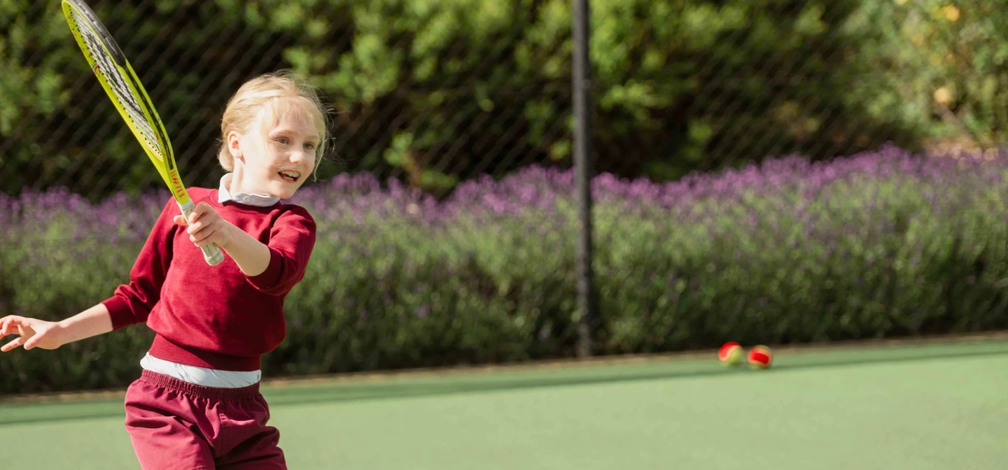 Child attending junior tennis coaching class, on tennis court swinging racket