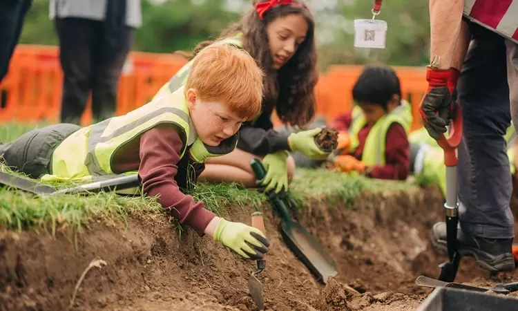 A child lies on the ground over the archaeology dig