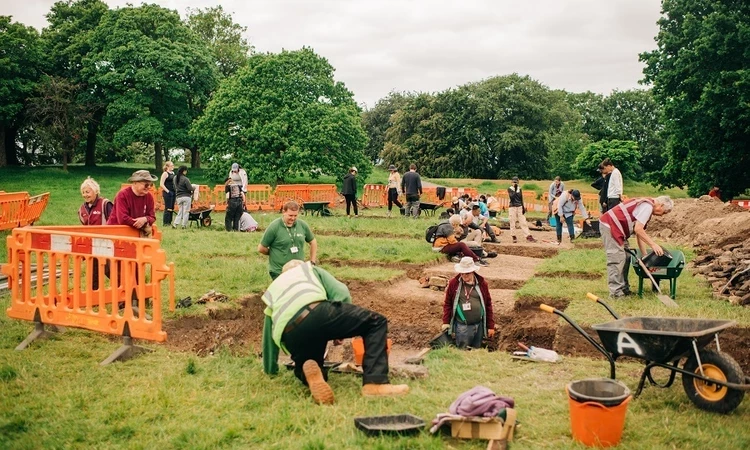 A view looking out over an archaeology dig with many people digging and surveying the ground.