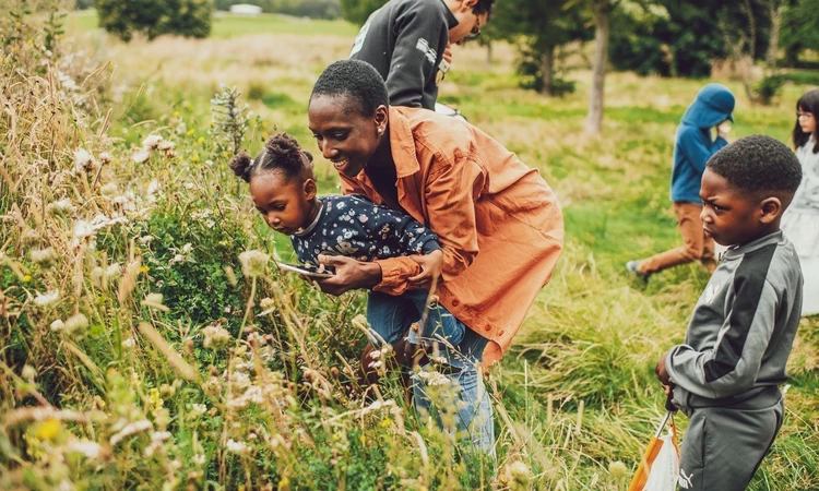 A mother and two young children looking closely at wildlife in tall grass