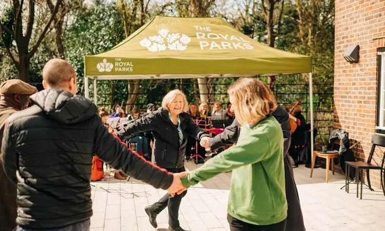 People are seen dancing in a ring outside the cafe with a Royal Parks branded gazebo in the background.