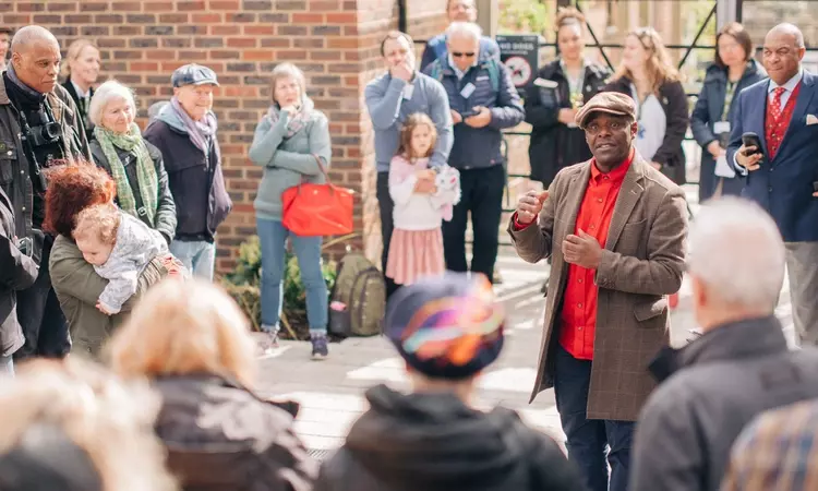 A crowd of people can be seen listening to Paterson Joseph as he reads from his book.