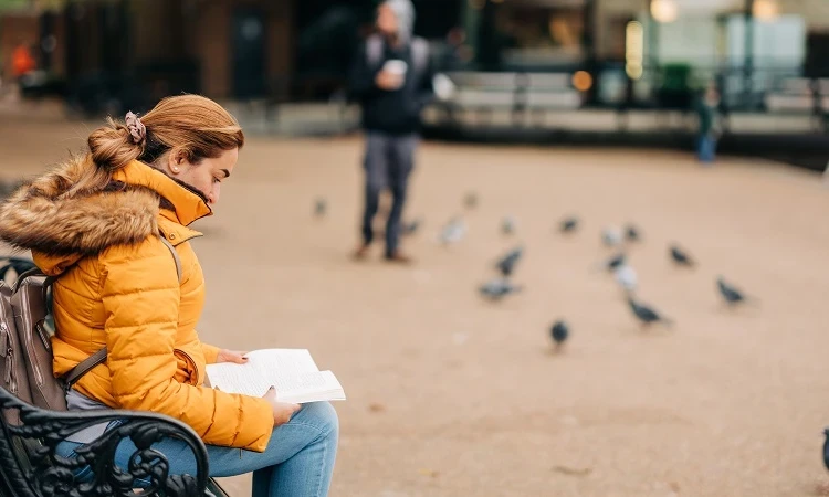 Woman reading a book on a park bench near the Serpentine Bar and kitchen