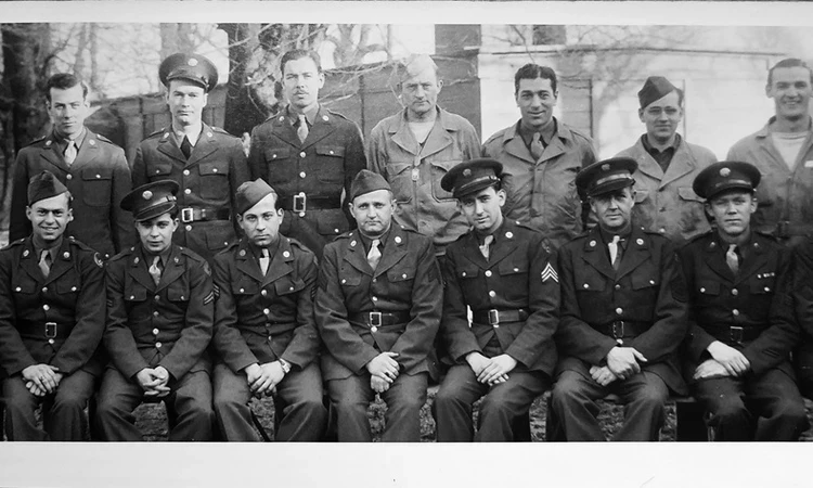 A black and white group image of Second World War United States airmen. Trees and huts in Bushy Park can be seen behind.