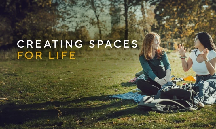 Two people sitting on grass on the right and the words Creating Spaces for Life on the left. 