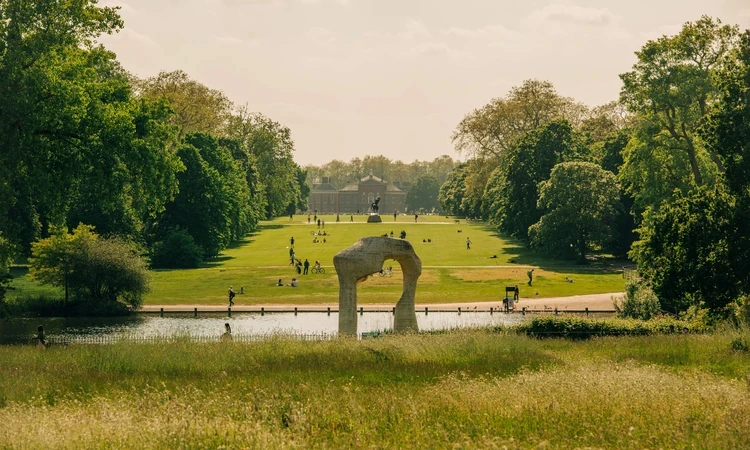 a wide shot of a green space with people and a lake in Kensington Gardens