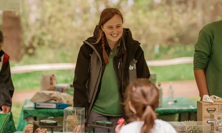 Image of 3 adults behind a desk, in an outdoor setting, explaining educational activities to a child.