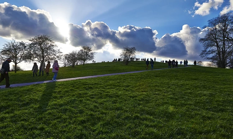 The sun setting behind the clouds at the top of a hill