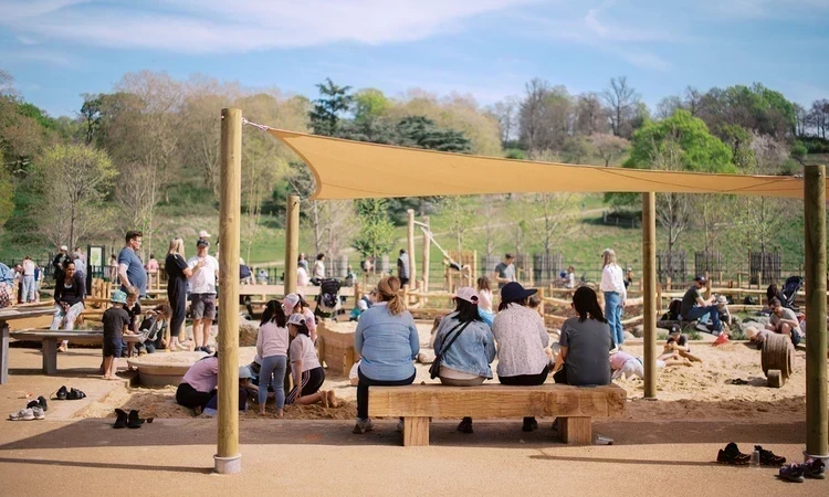 Parents on covered seating watch their children playing in a sandpit