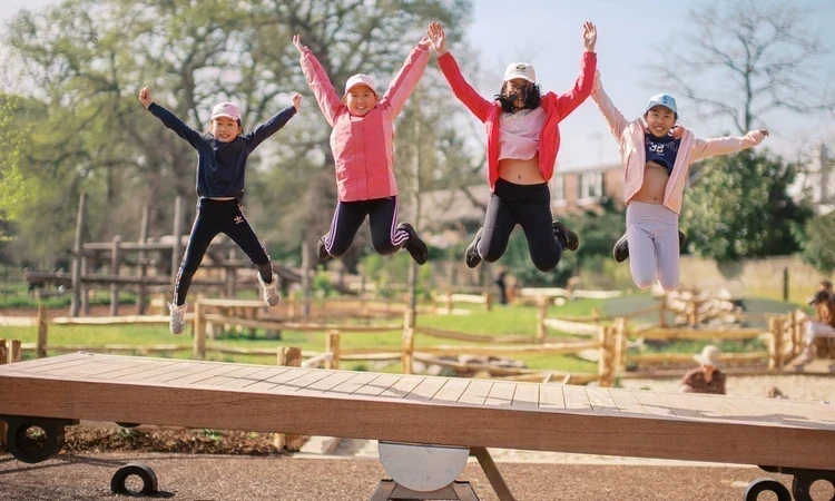Four girls jumping above a giant see-saw