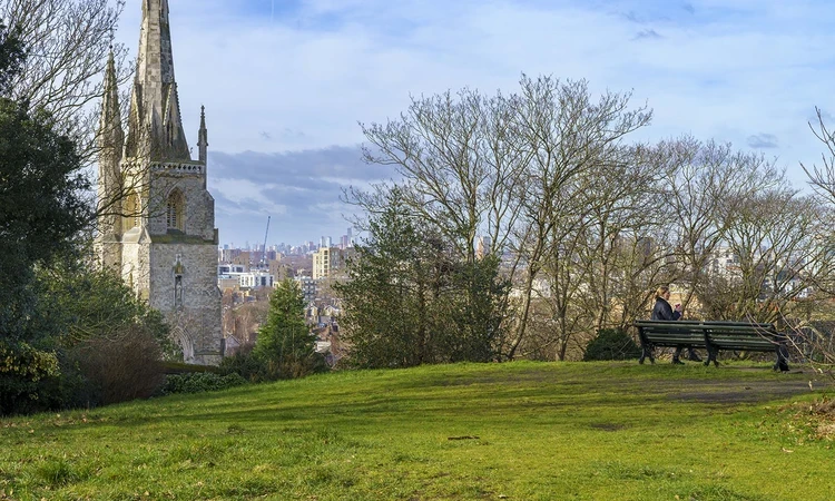 Woman sitting on a park bench, with a church in the background.