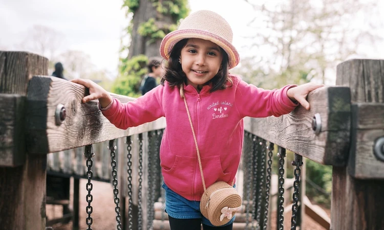 A young girl in a hat crossing a playground bridge