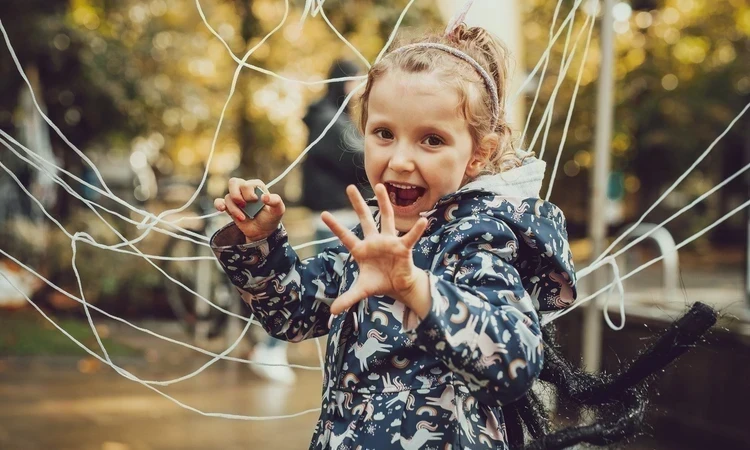 A girl, wearing a spider costume is doing a playful scary pose in front of a big cobweb made of string