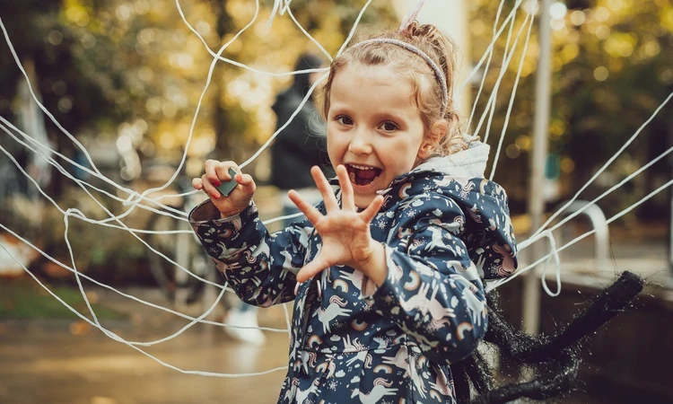A girl, wearing a spider costume is doing a playful scary pose in front of a big cobweb made of string