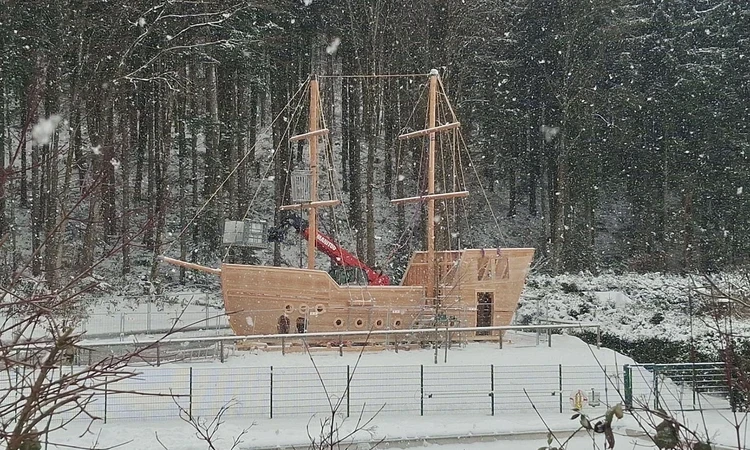 A wooden playground 'galleon' being constructed in front of a snowy forest