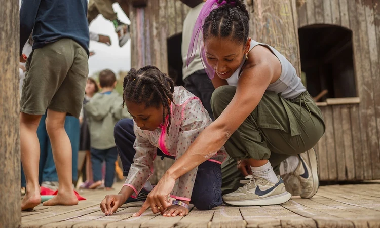A mother and daughter create a design on the ground using coloured chalk