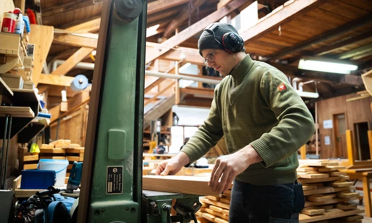 A man in a workshop sanding wood on a machine