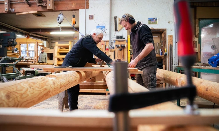 Two men in a carpentry workshop working on a large timber frame