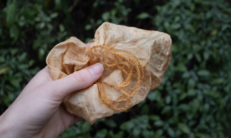 Hand holding orange lichen dyed fabric and yarn