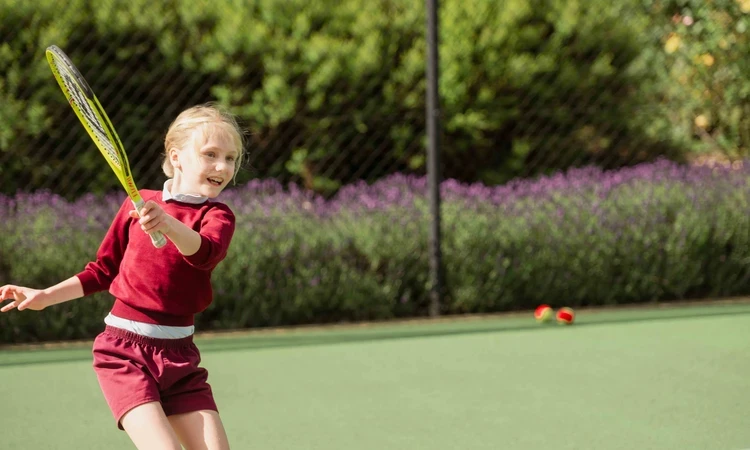 Child attending junior tennis coaching class, on tennis court swinging racket