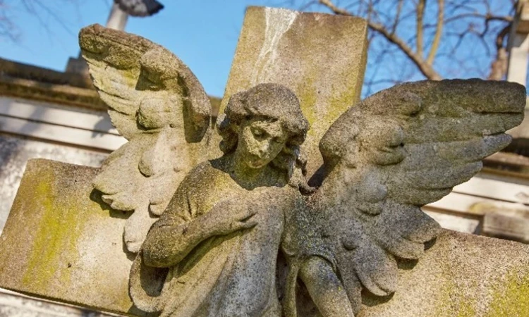 closeup image of an angel stature on a cross with her hand on her heart and wings spreading out behind