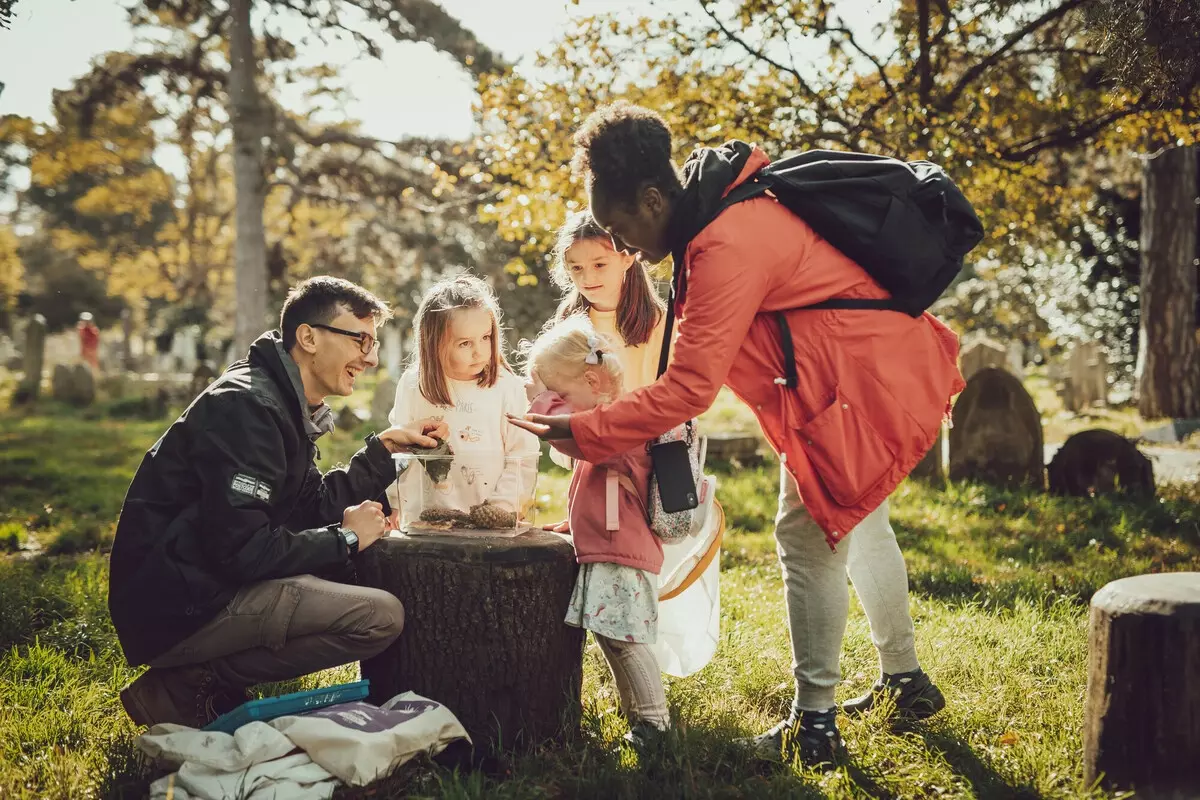 A group of adults and children curiously looking inside a plastic box in a park