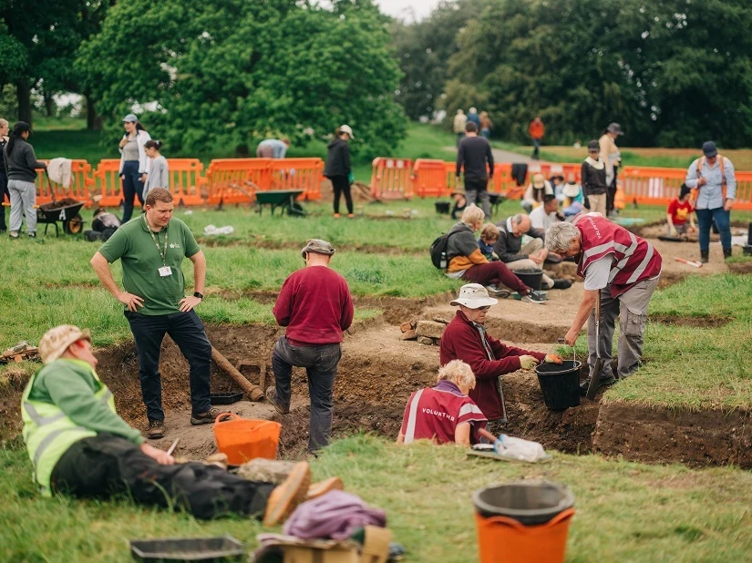 A view looking out over an archaeology dig with many people digging and surveying the ground.