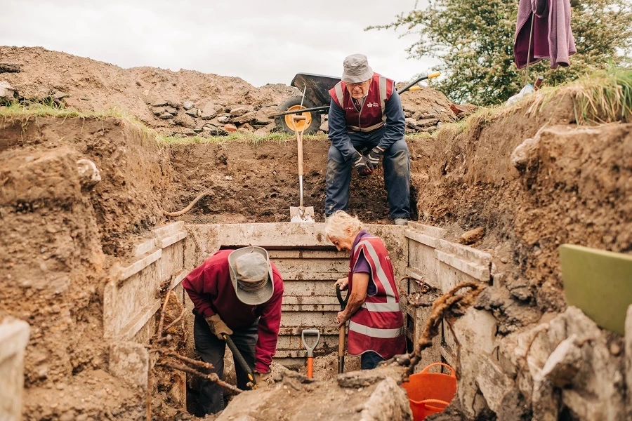 A view from inside the air raid shelter looking across at three volunteers digging earth.