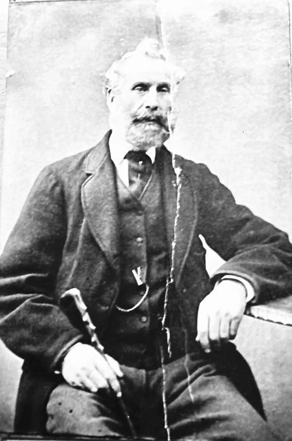 A black and white photographic portrait of Angus Duncan Webster, he sits clutching a cane in a formal suit
