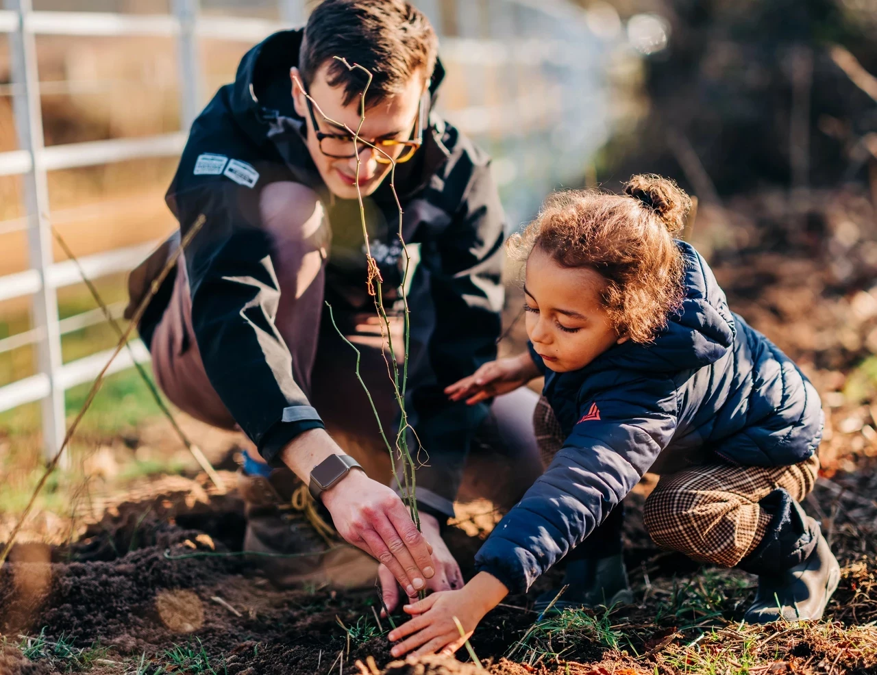 Image of a man helping a young child plant a sapling.