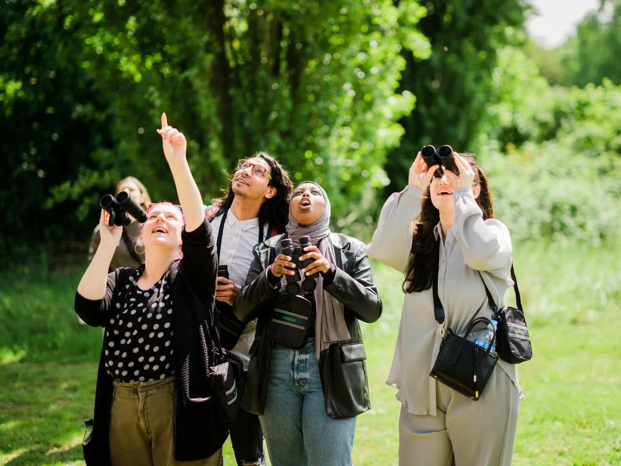 Four women in an outdoor setting observing nature through binoculars.