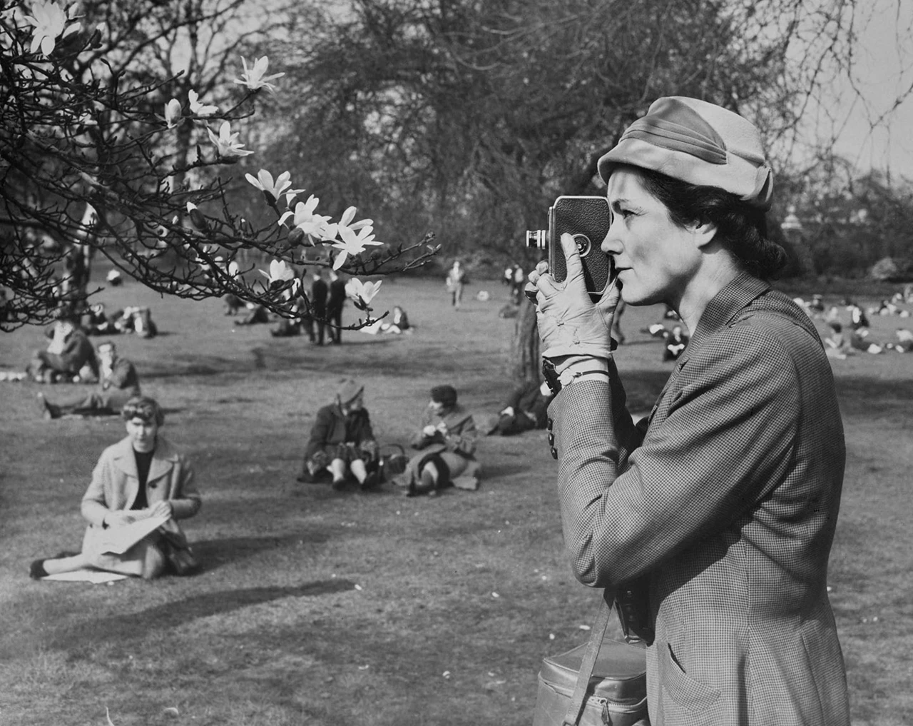 A woman in a hat taking a photograph of spring blossom
