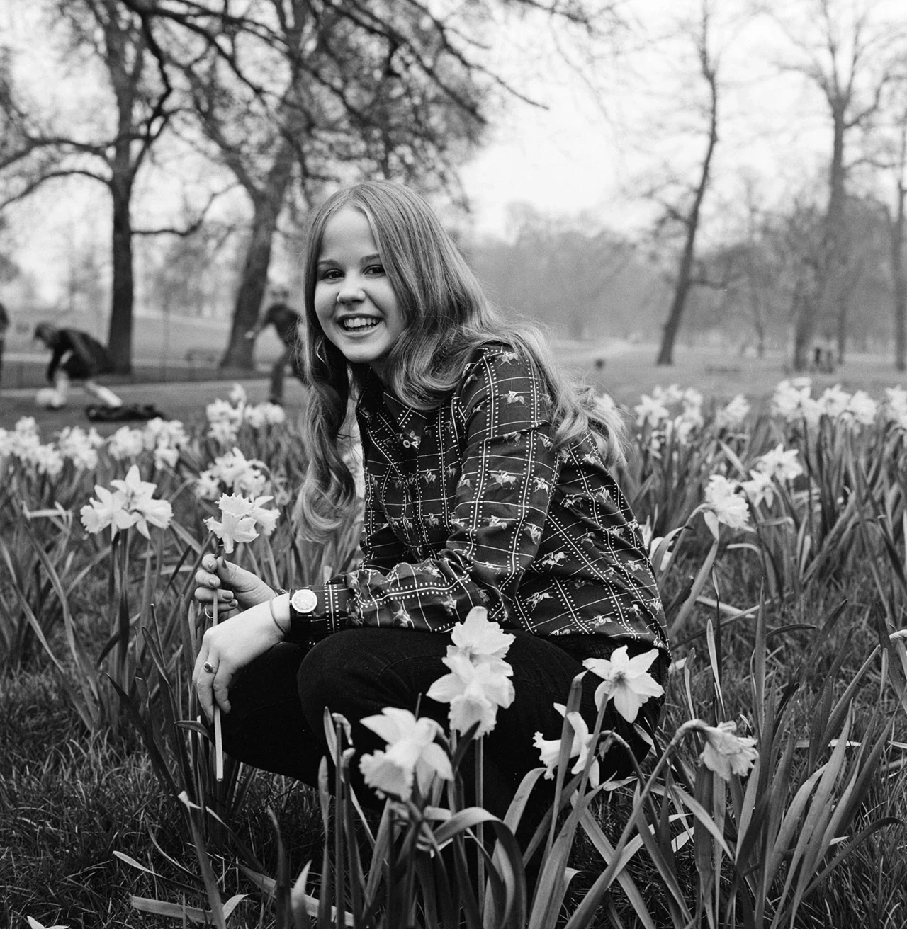 A teenage girl crouches for a photo among daffodils