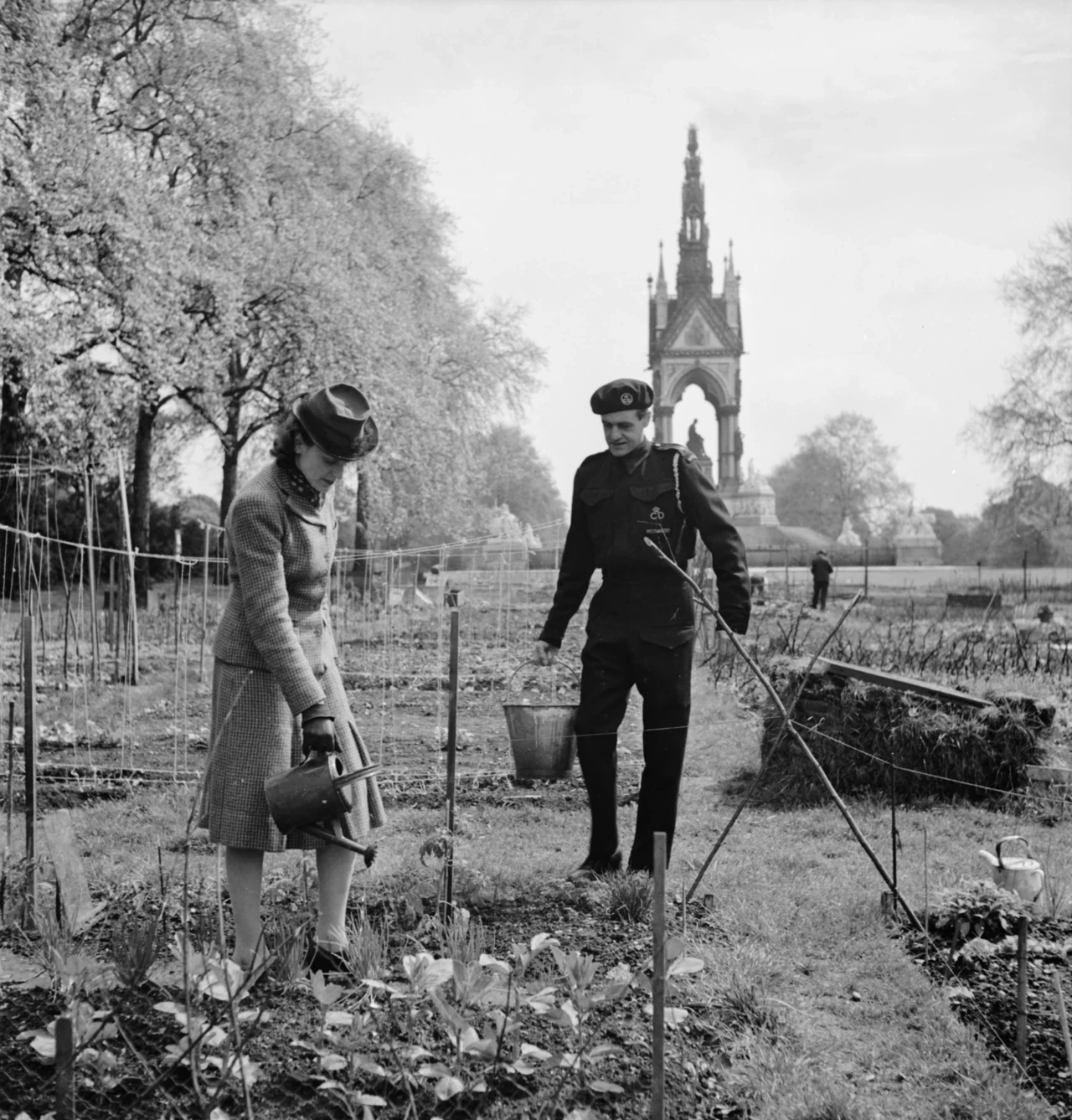 A woman waters her vegetables in Kensington Gardens with the help of a Westminster Civil Defence Warden