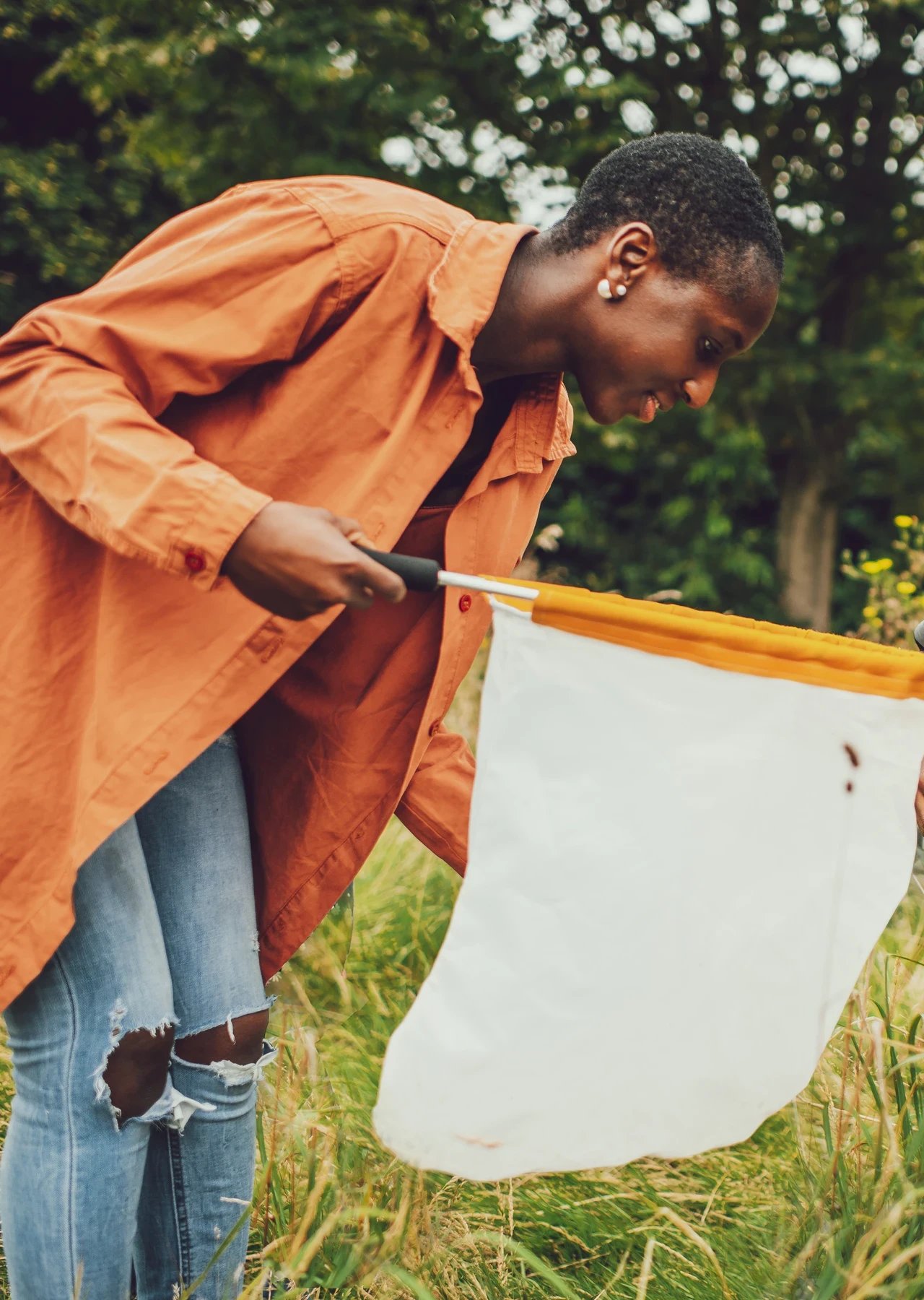 A woman using a sweep net to look at insects in the long grass