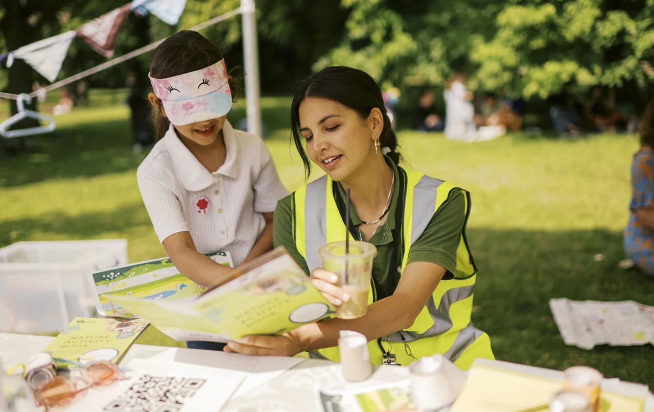 The Royal Parks' Cassie reads to a child at a Play in The Park session