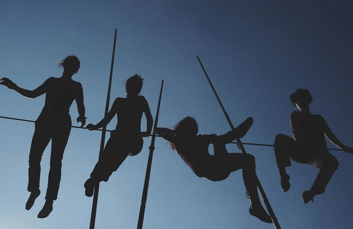 Silhouette image of circus performers on ropes and poles, against a blue sky.
