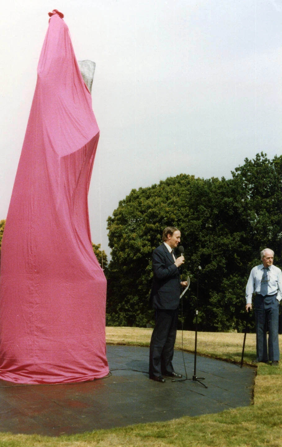 The sculpture, hidden by a red sheet, at its unveiling. Henry Moore watches on.